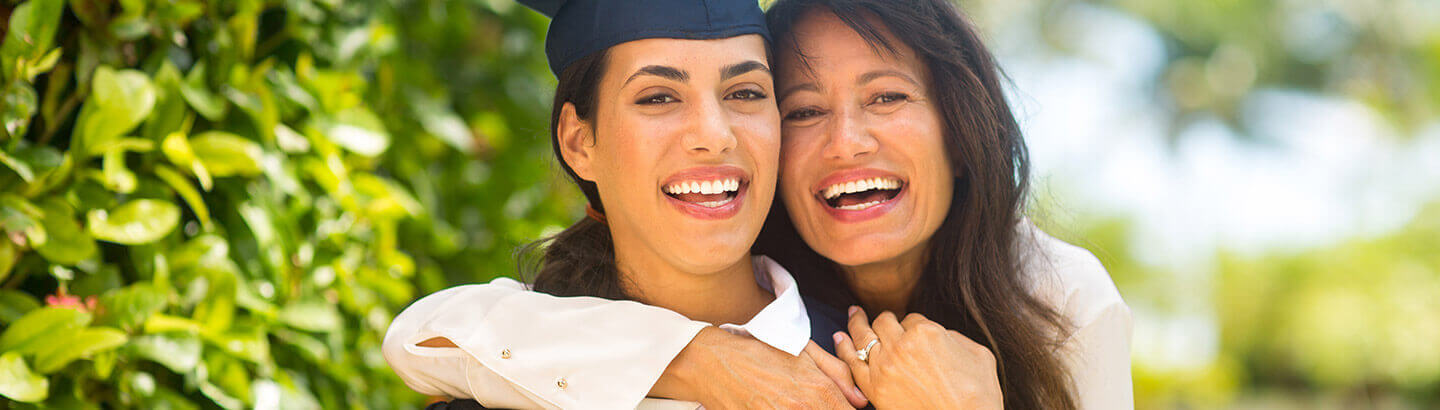 Mamá abrazando sonriente a su hija graduada por lograr ahorro para estudios universitarios