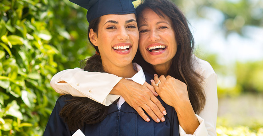 Mamá abrazando sonriente a su hija graduada por lograr ahorro para estudios universitarios