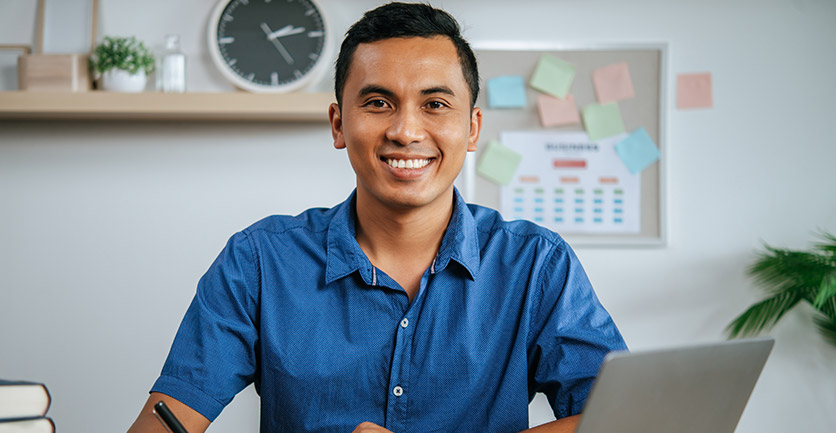 Hombre latino sonriente en su portátil aprendiendo sobre Que es la compra de cartera